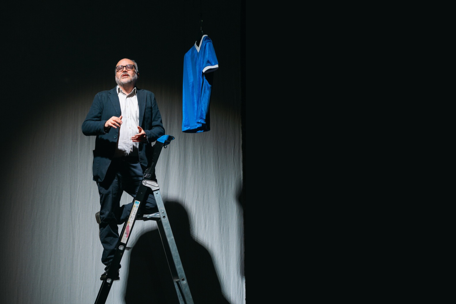 un uomo sale su una scala davanti al sipario per raggiungere una maglia da calciatore del mitico maradona