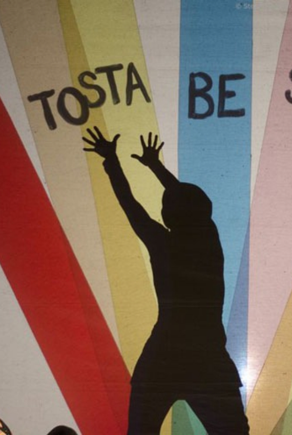 una sagoma umana allunga le mani verso un murales a strisce colorate